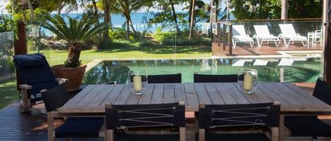 Una terraza de madera con una mesa y sillas, con vista a una piscina y al océano.