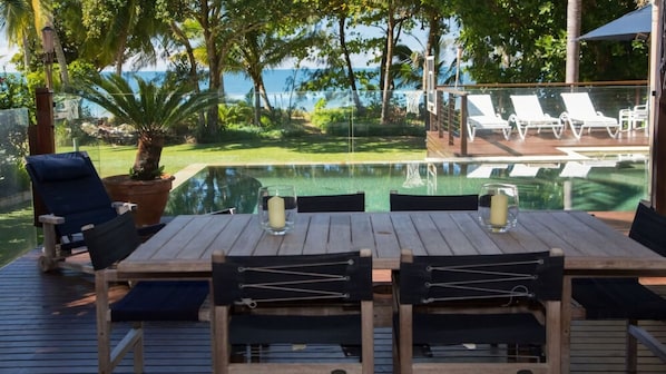 A wooden deck with a table and chairs, overlooking a pool and a view of the ocean.