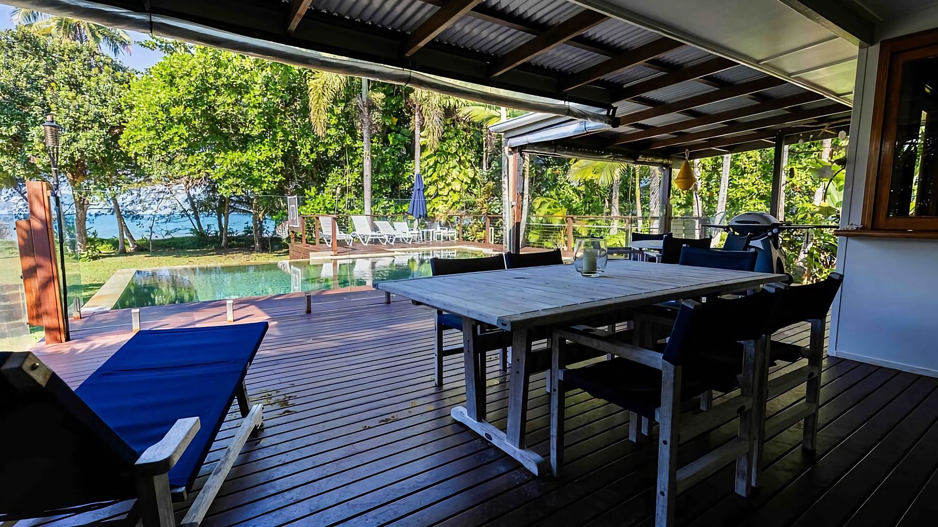Una terraza exterior con piscina, muebles de madera y vista al mar.