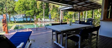 Una terraza exterior con piscina, muebles de madera y vista al mar.