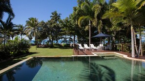 A clear pool with a deck, lounge chairs, and a view of the ocean. - The Beach Cottage - Absolute Beachfront (Wongaling Beach)