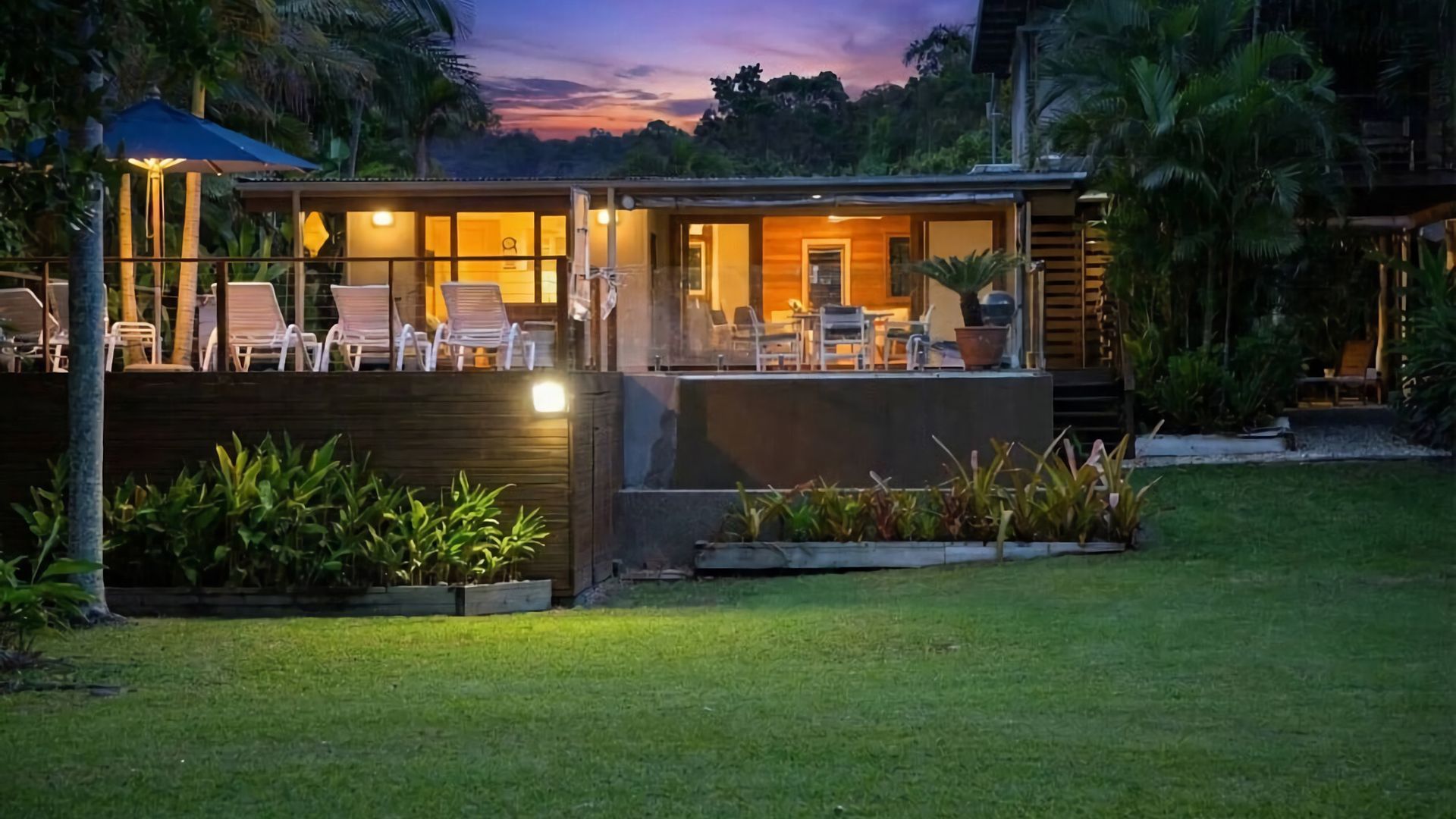 Un espacio lounge exterior moderno con asientos y piscina, rodeado de exuberante vegetación.