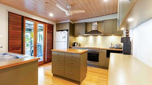 A modern kitchen with wooden cabinets, a built-in oven, and a large island with a sink. - The Beach Cottage - Absolute Beachfront (Wongaling Beach)