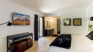 Ein Schlafzimmer mit Bett, Schreibtisch, Stuhl, Kleiderschrank und einem durch eine offene Tür einsehbaren Badezimmer.