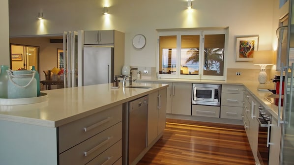 A modern kitchen with a central island, built-in appliances, and a view of the outdoors through a window. - Ripples on the Beach (Mission Beach)
