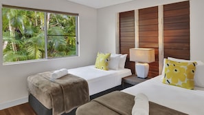 A hotel room with two beds, a window with a view of greenery, a wooden headboard, and a bedside lamp. - Ripples on the Beach (Mission Beach)