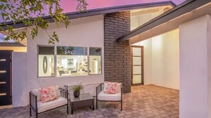 A modern house with a patio area featuring two sofas and a table, a brick wall, and large windows.
