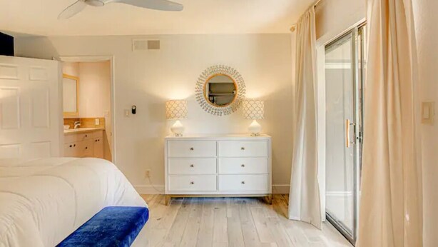 Ein Schlafzimmer mit einem Bett, einer weißen Kommode, einem Spiegel und einem Deckenventilator.