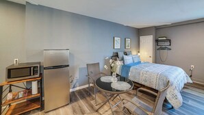 A compact bedroom with a bed, bedside table, and a small kitchenette area including a refrigerator and microwave. - Spacious Studio with Private Entry (Moreno Valley)