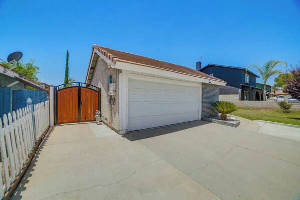 A garage with a white door, a wooden gate, and a satellite dish on the left. - Spacious Studio with Private Entry (Moreno Valley)