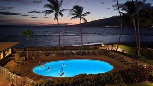 Une piscine où se trouvent trois personnes, entourée de palmiers et offrant une vue sur l’océan au crépuscule.