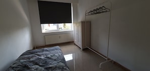 Makuuhuoneessa on sänky, patteri, vaatekaappi ja ikkuna, jossa on musta pimennysverho.