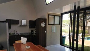 A modern kitchen with dark cabinetry, a wooden dining table, and a view of a swimming pool through large glass doors. - Relax beach house at 10 min from the best beaches in Costa Rica (Provincia de Guanacaste)