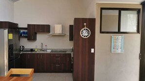 A compact kitchen with dark wooden cabinets, a stainless steel refrigerator, and a built-in oven. There is a wooden dining table and bench, and a wall-mounted clock. - Relax beach house at 10 min from the best beaches in Costa Rica (Provincia de Guanacaste)