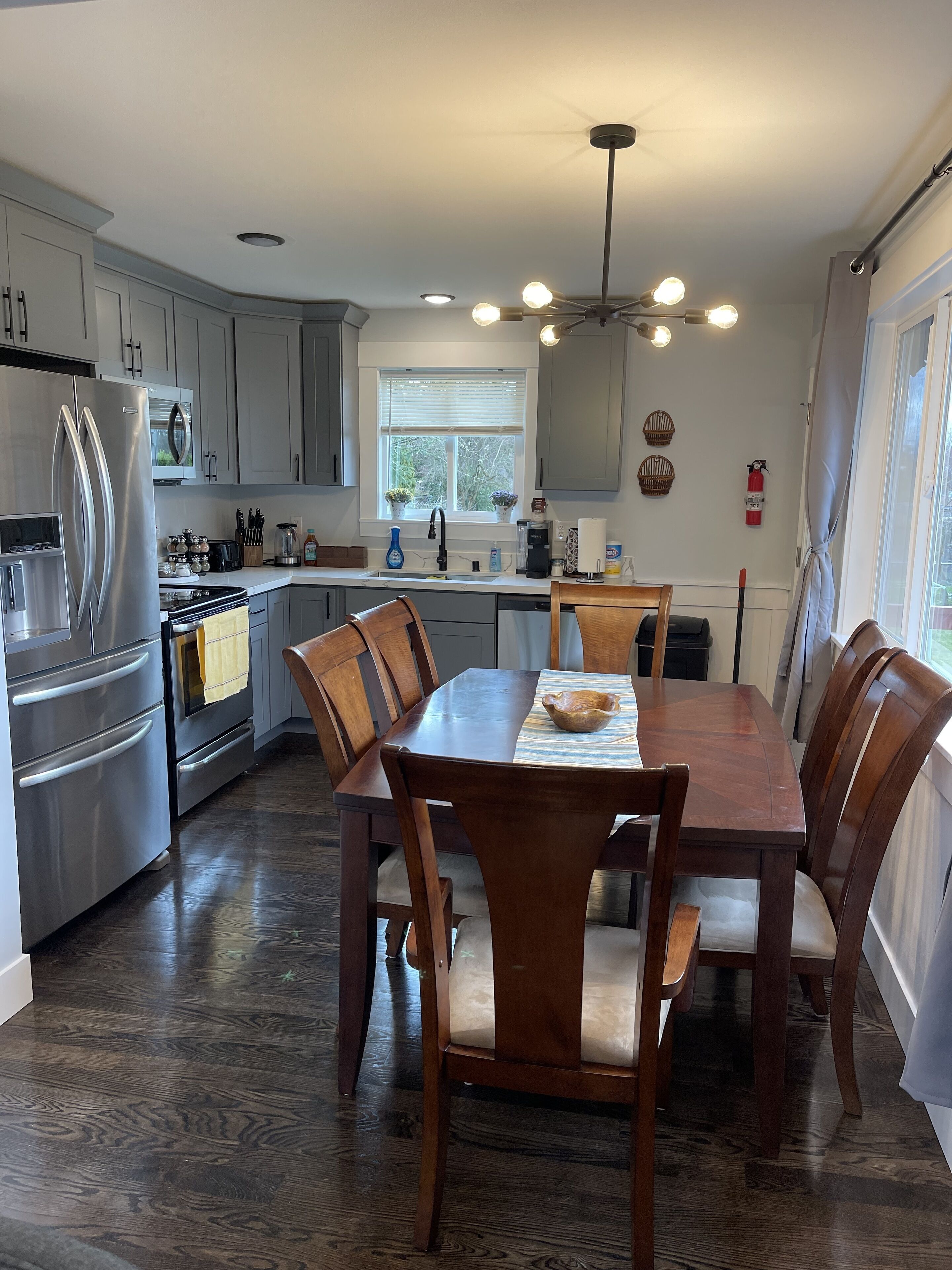 A modern kitchen with stainless steel appliances, a dining table with chairs, and a window with blinds.