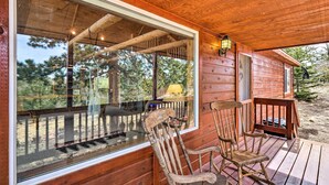 A wooden cabin with a large window, a porch with rocking chairs, and a visible deck.