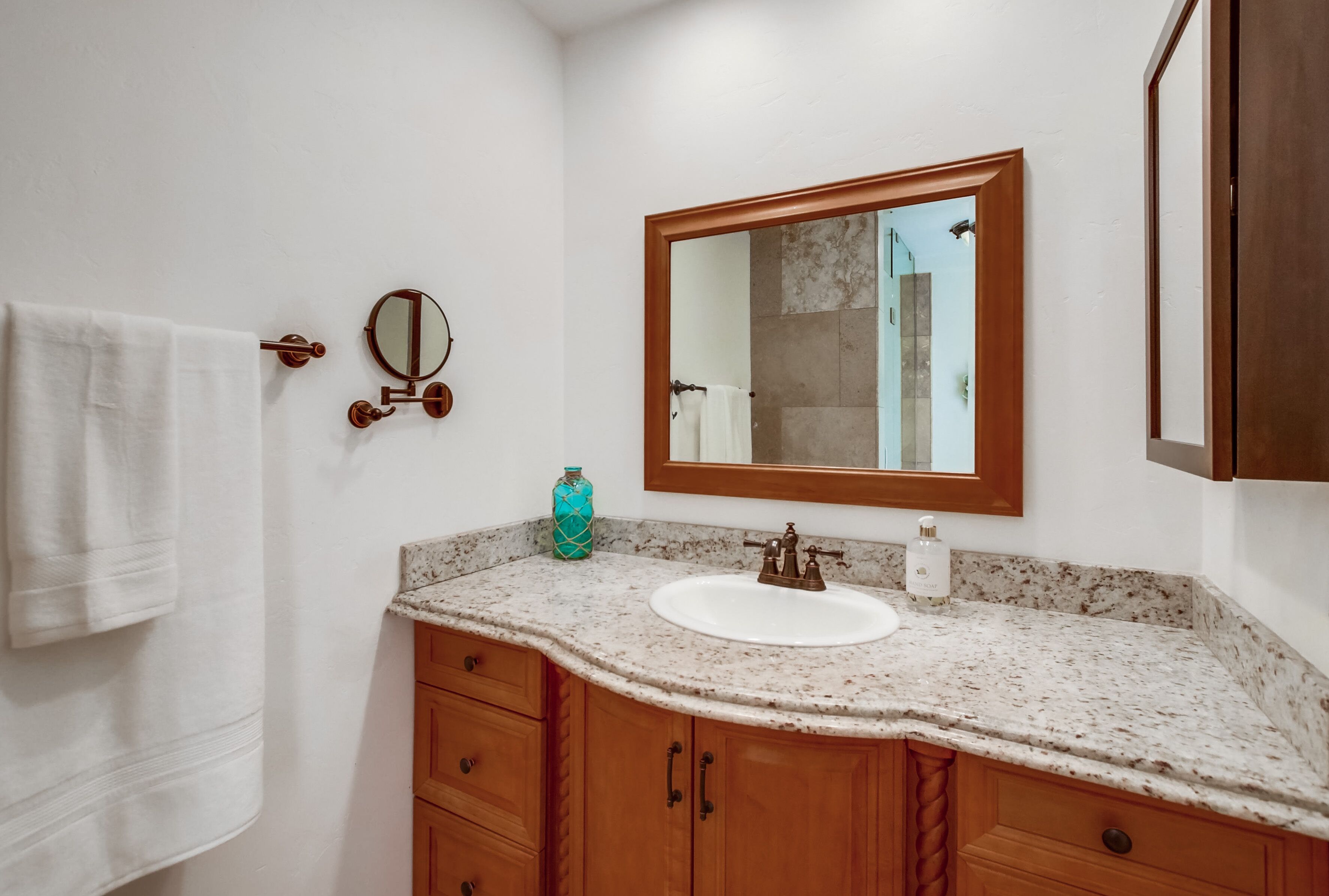 A bathroom with a white sink, wooden cabinets, a mirror, and a towel hanging on the wall.