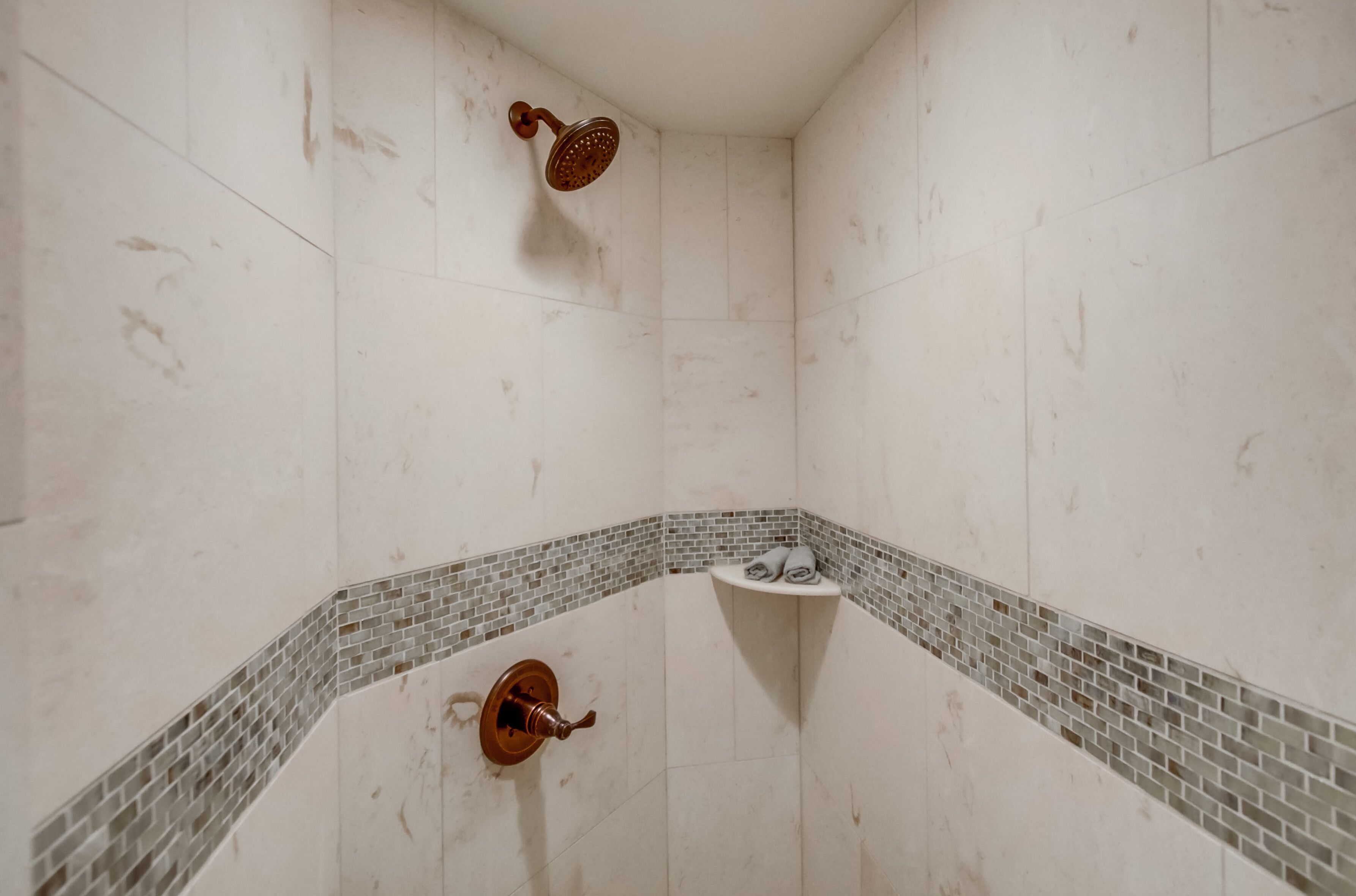 A shower with a handheld showerhead, a corner sink with a small shelf, and a tiled floor.