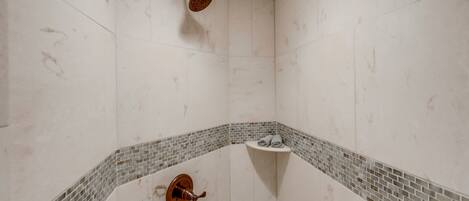 A shower with a handheld showerhead, a corner sink with a small shelf, and a tiled floor.