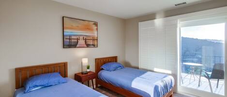A hotel room with two beds, a painting on the wall, a nightstand, and a view of the outdoors through a large window.