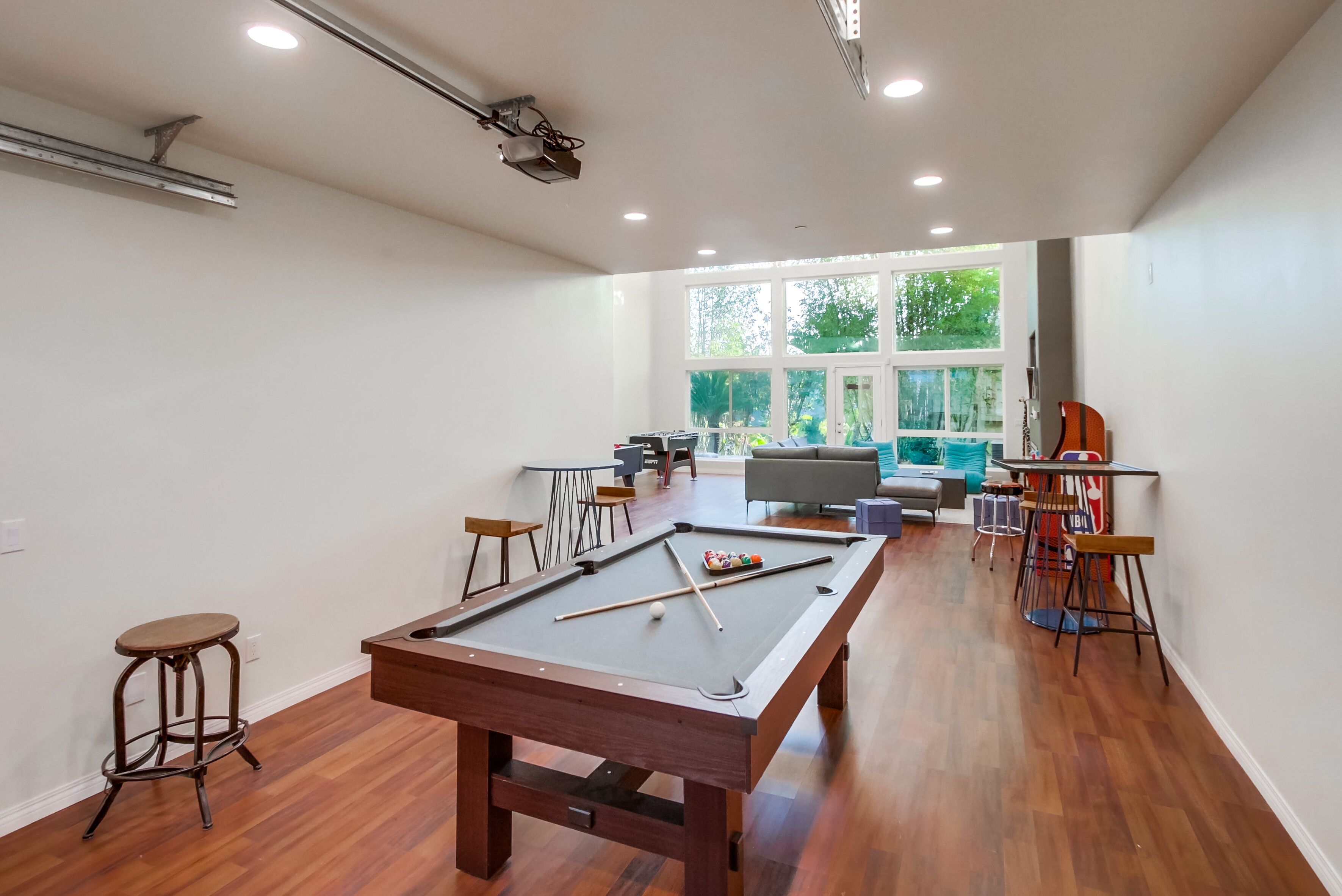 A spacious room with a pool table, bar stools, and a seating area with a couch and chairs.