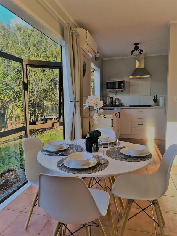A dining area with a table set for four, a kitchen with modern appliances, and a view of a garden through large windows.