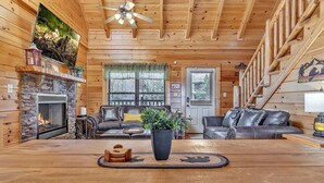 L’intérieur chaleureux d’un chalet en bois, avec une cheminée en pierre, des canapés en cuir et une table à manger en bois.