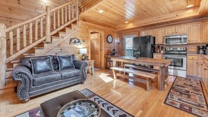 L’intérieur d’un chalet en bois comprend un escalier, un canapé en cuir, une table à manger et un coin cuisine.
