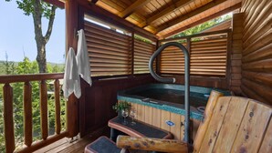 Une terrasse en bois avec un jacuzzi, deux chaises et une serviette suspendue à la rambarde.