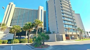 A modern hotel with multiple floors, a flat roof, and a parking area with palm trees. -  Oceanfront  ★Double Queen ★Pool & Lazy River★Private Balcony ★ Kitchenette (Myrtle Beach)