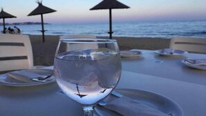 A table with a glass of water, plates, and napkins at a beachside restaurant with umbrellas. - Nuevo, con Grande Terraza, a 200 m de la Playa y 500m del Puerto y Centro (Cambrils)