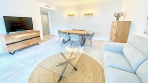 A modern living room with a TV, wooden entertainment unit, dining table with chairs, and a light-colored sofa. - Nuevo, con Grande Terraza, a 200 m de la Playa y 500m del Puerto y Centro (Cambrils)