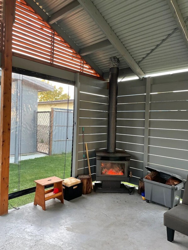 A covered outdoor area with a wood-burning stove, a wooden bench, and a concrete floor.