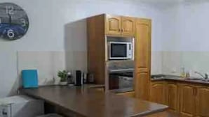 Una cucina con mobili in legno, un forno a microonde, un piccolo frigorifero e un orologio a parete.