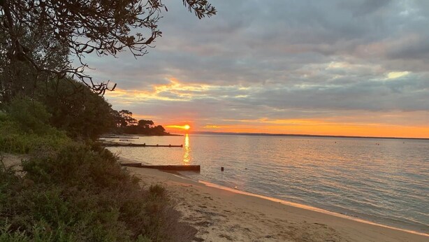Una spiaggia al tramonto, con acque calme e un litorale roccioso.