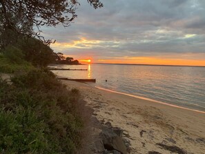 A beach with a sunset, calm water, and a rocky shoreline.