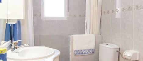 A bathroom with a sink, toilet, shower, and a window.