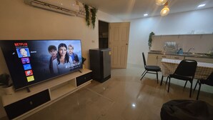 Un soggiorno con TV che mostra un profilo Netflix, un'area pranzo con tavolo e sedie e una zona cucina con lavello e pensili.