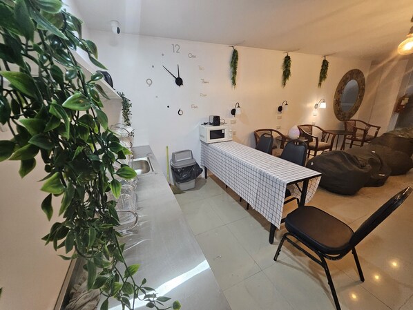 A modern dining area with a long table, chairs, a clock, and hanging plants.