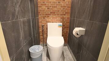 A small, tiled bathroom with a toilet, a trash bin, and a paper towel dispenser.