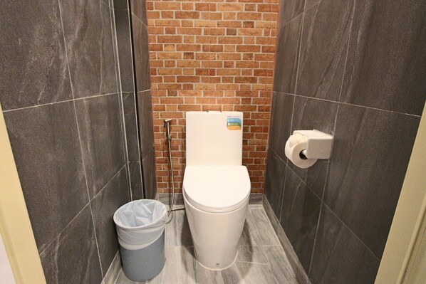 A small, tiled bathroom with a toilet, a trash bin, and a paper towel dispenser. - Jomtien Beach Hostel - Soi 7 Prime Spot - 200m to Beach next to Food Market (Pattaya)