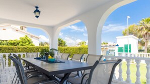 Een terras buiten met een tafel en stoelen, omgeven door witte zuilen en een witte hekken.