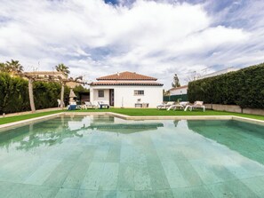 A house with a swimming pool, a pergola, and a well-maintained lawn.