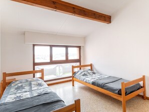 Two bunk beds are arranged in this compact room with a window and a wooden beam above.