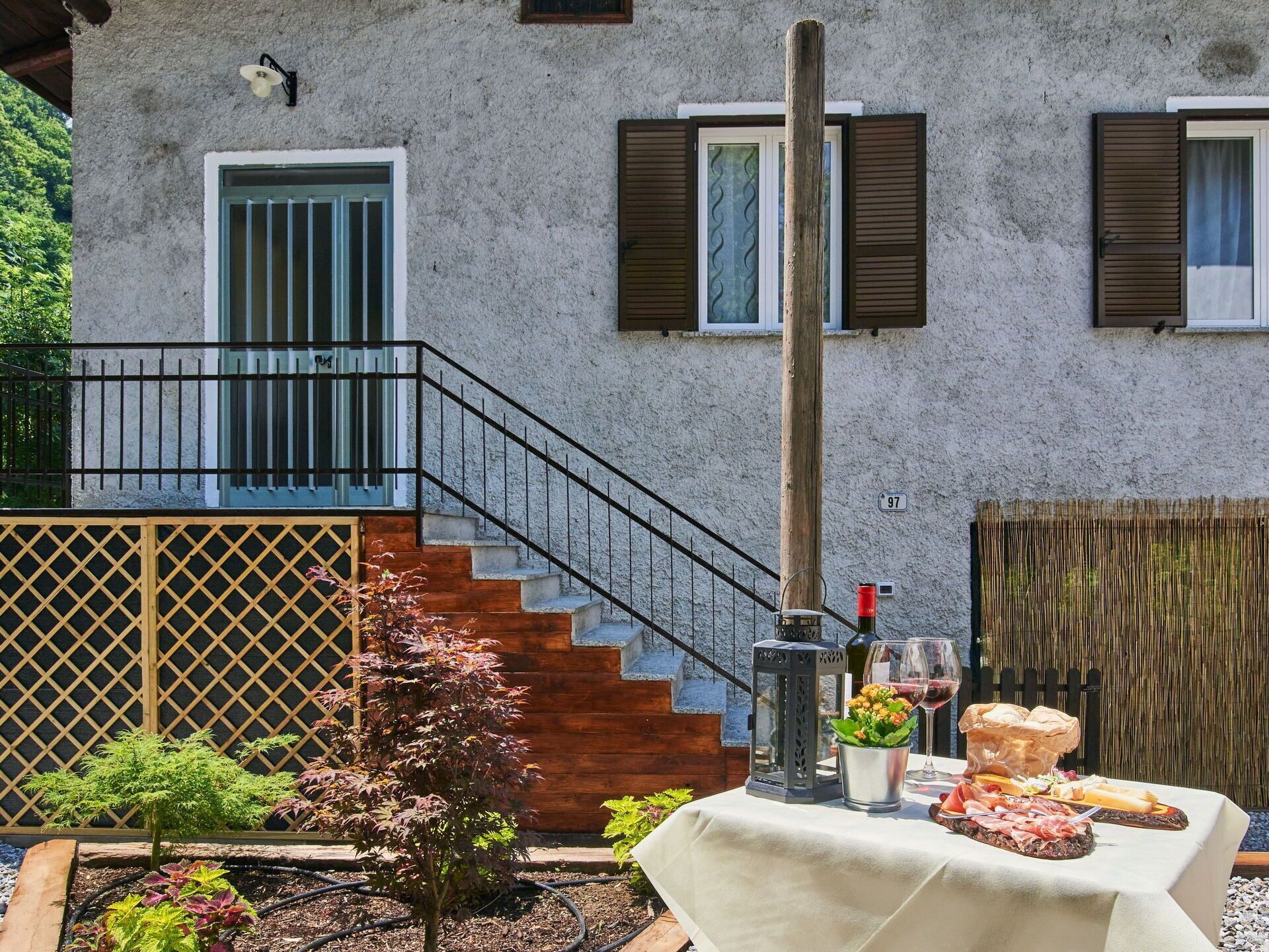 A patio with a table set for a meal, a staircase, and a building with a textured wall and shutters.