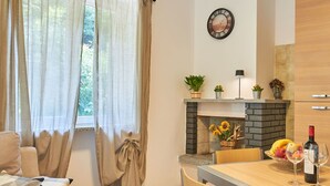 A living room with a sofa, a dining table with chairs, a fireplace, and a clock on the wall.