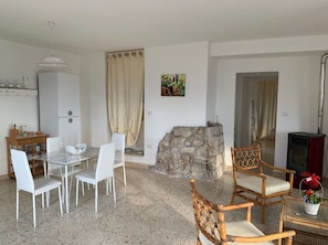 A dining area with a stone wall, a table with chairs, a wooden chair, and a small table with a basket of flowers. - Beautiful apartment for 4 guests with A/C, WIFI, TV, patio and pets allowed (Matino)
