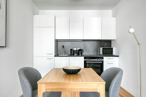 A modern kitchen with white cabinets, a wooden table, and two grey chairs.