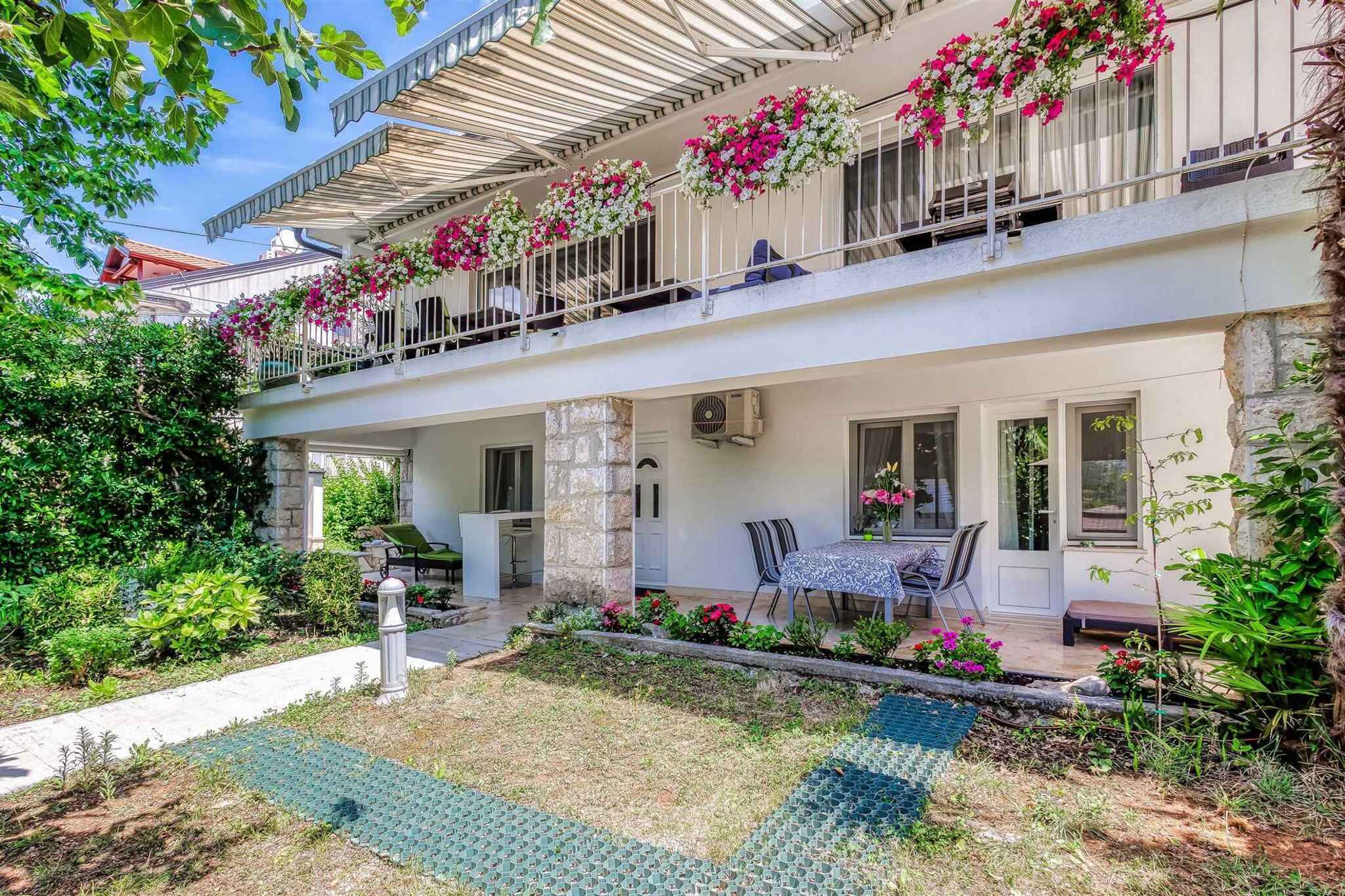 A two-story building with a balcony adorned with flowers, a covered outdoor seating area, and a garden with a mosaic pathway.