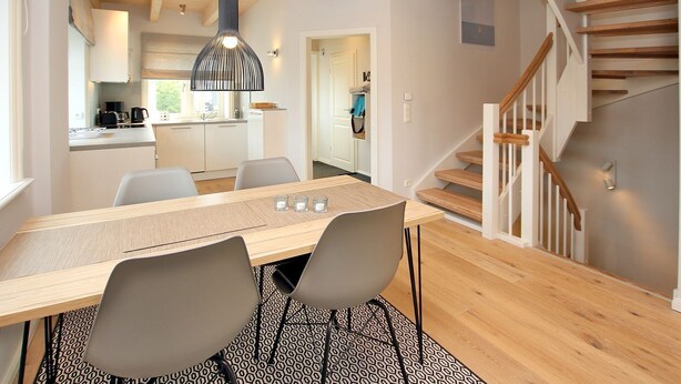 Una cocina moderna con armarios blancos, una mesa de comedor de madera y una escalera con barandillas de madera.